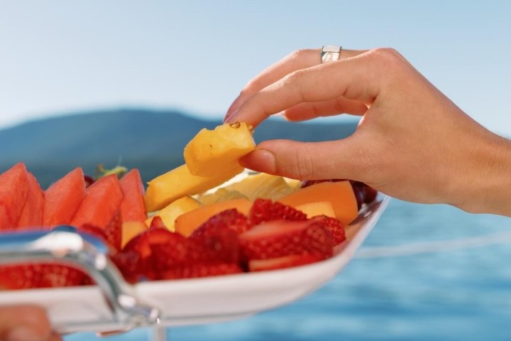 Hand picking fruit from a plate with a scenic water view.