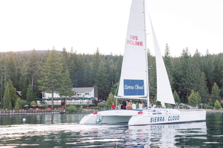Catamaran named Sierra Cloud sailing on a lake with forested shore and buildings in background.