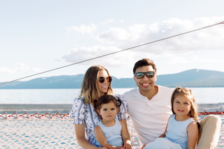 Family sitting on a net with sea and mountains in background.