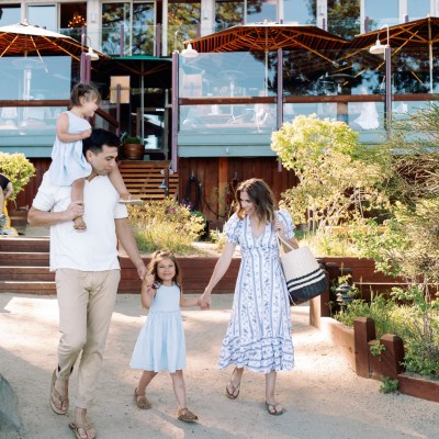 Family walking outdoors in front of a building, child on shoulder.