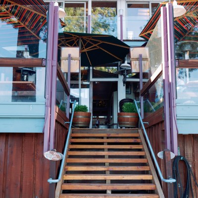 Wooden stairs leading to a patio with umbrellas and glass railings.