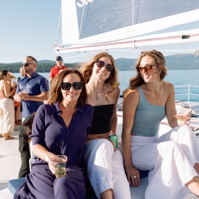 Three people sitting on a boat deck, smiling, with drinks in hand.
