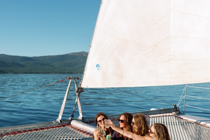 Four people on a sailboat, sitting and toasting drinks on a sunny day.