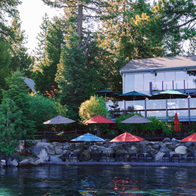 Lakeside restaurant with colorful umbrellas and surrounding trees.