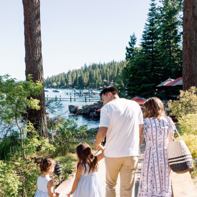 Family walking toward lakeside area with trees and clear sky.