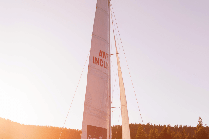 People on a catamaran with tall sails, sailing on a lake at sunset.