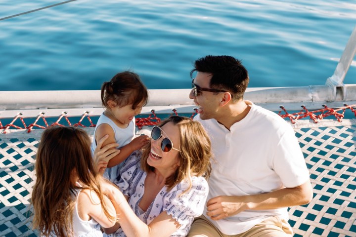 Family sitting on boat net over water, smiling and interacting.