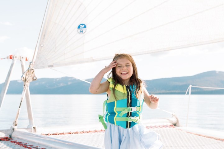 Girl on a sailboat trampoline, wearing a life jacket, with a sail in the background.
