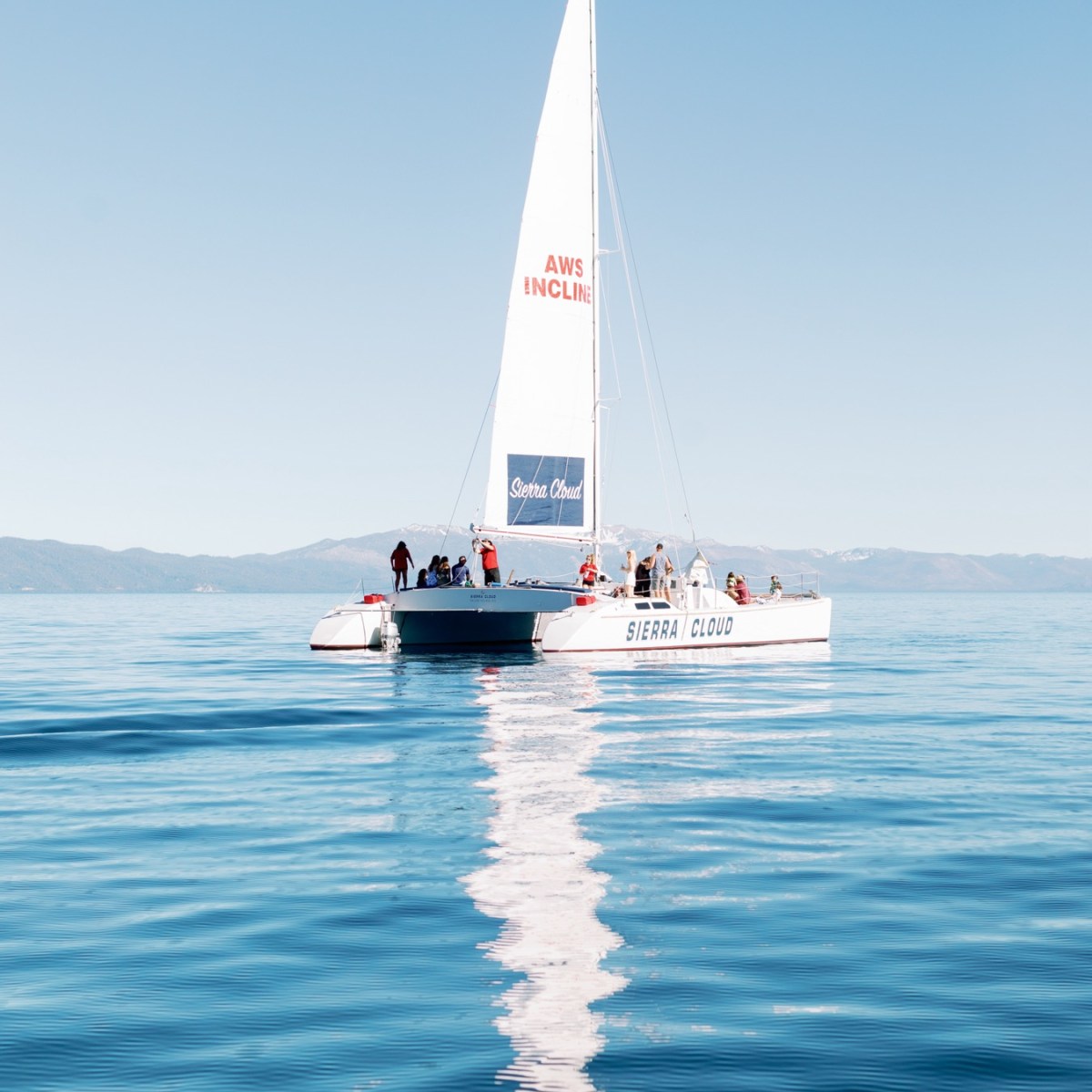 Sailboat with people on calm blue water under a clear sky.