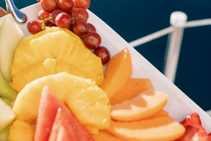 Tray of assorted fruits including pineapple, grapes, and watermelon against a blue background.