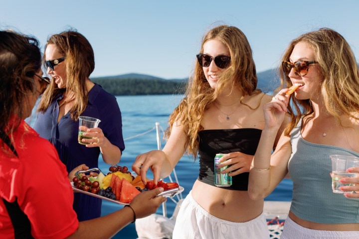 Group of people on a boat enjoying drinks and snacks, with a lake in the background.