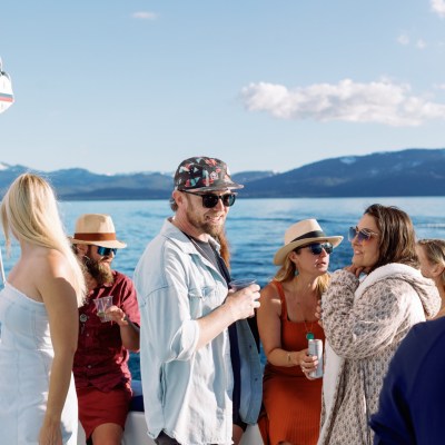 Group of people socializing on a boat in sunny weather with mountains in the background.