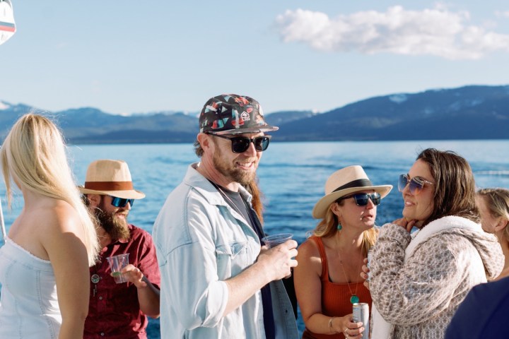 Group of people socializing on a boat in sunny weather with mountains in the background.