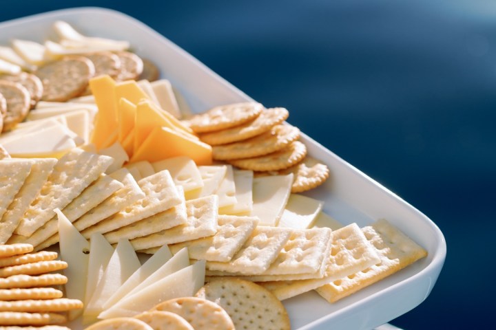 Assorted crackers and cheese slices on a tray with a sea background.