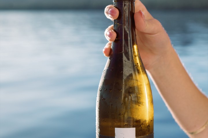 Person holding Lost Sierra wine bottle with corkscrew by a lake