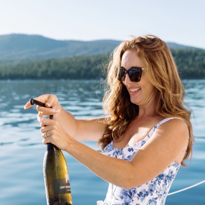 Woman opening champagne bottle on a boat with lake and mountain view.