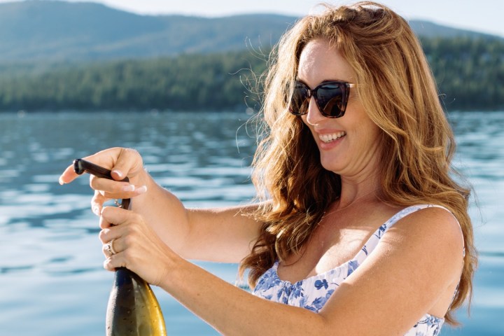 Woman opening champagne bottle on a boat with lake and mountain view.