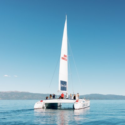 Sailboat on calm waters with people onboard, clear sky, distant hills.